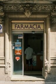 Architectural details of a historic pharmacy entrance in Madrid, Spain, featuring a lone customer inside.