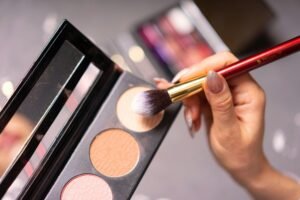 Hand with manicured nails using a makeup brush on a palette for cosmetic application.