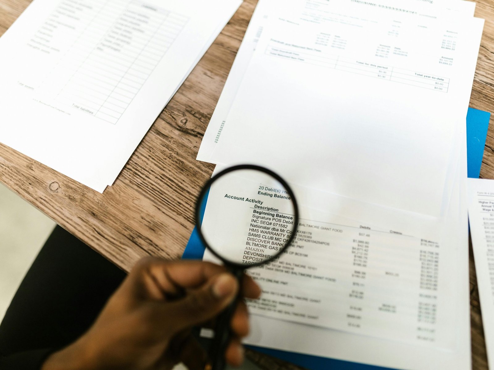 Close-up of hand using magnifying glass to review documents. Ideal for financial themes.