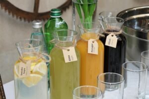 Vibrant assortment of fresh juices in labeled glass bottles with water bottles and glasses arranged outside on a table.